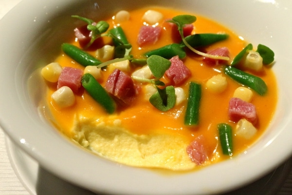 a half eaten dish of food with creamy custard covered with orange sauce and vegetables