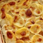 Closeup of French potato gratin dauphinois with bubbly browned top in a casserole dish.
