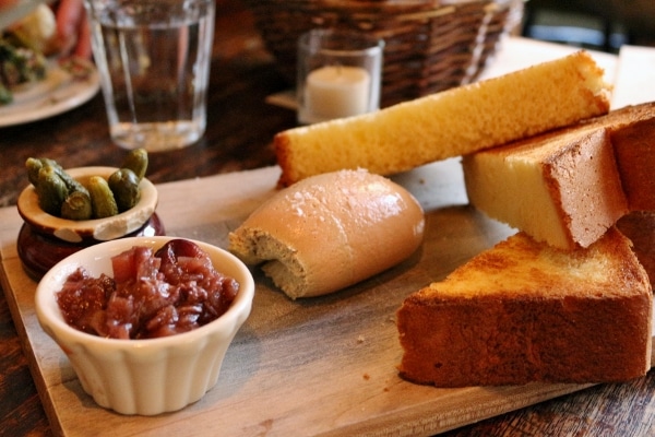 a closeup of a wooden board of pate served with toast and little cups of toppings