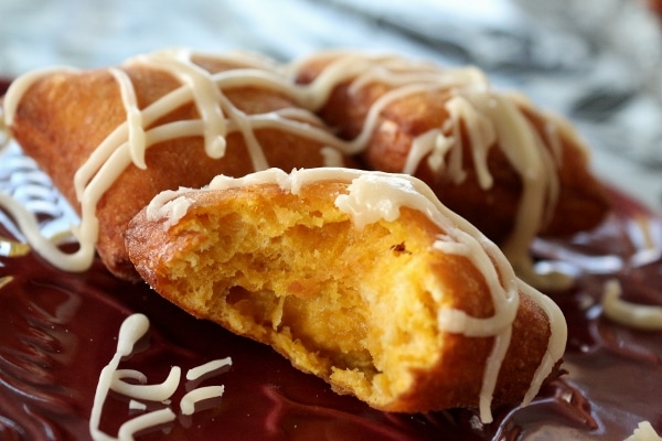 A closeup of a bitten pumpkin beignet on a dark red plate