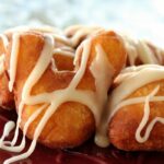 A closeup of a Mickey Mouse shaped fried beignet drizzled with white glaze