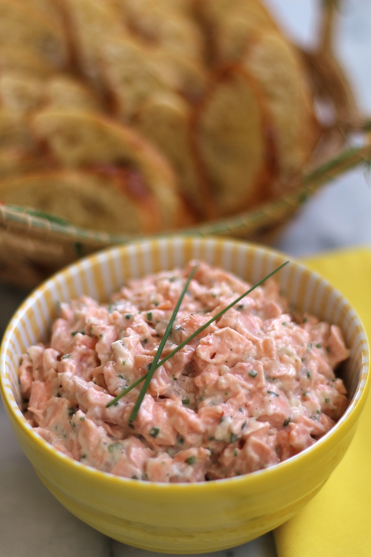 bowl of salmon rillettes garnished with chives, a basket of toasted baguette slices in background