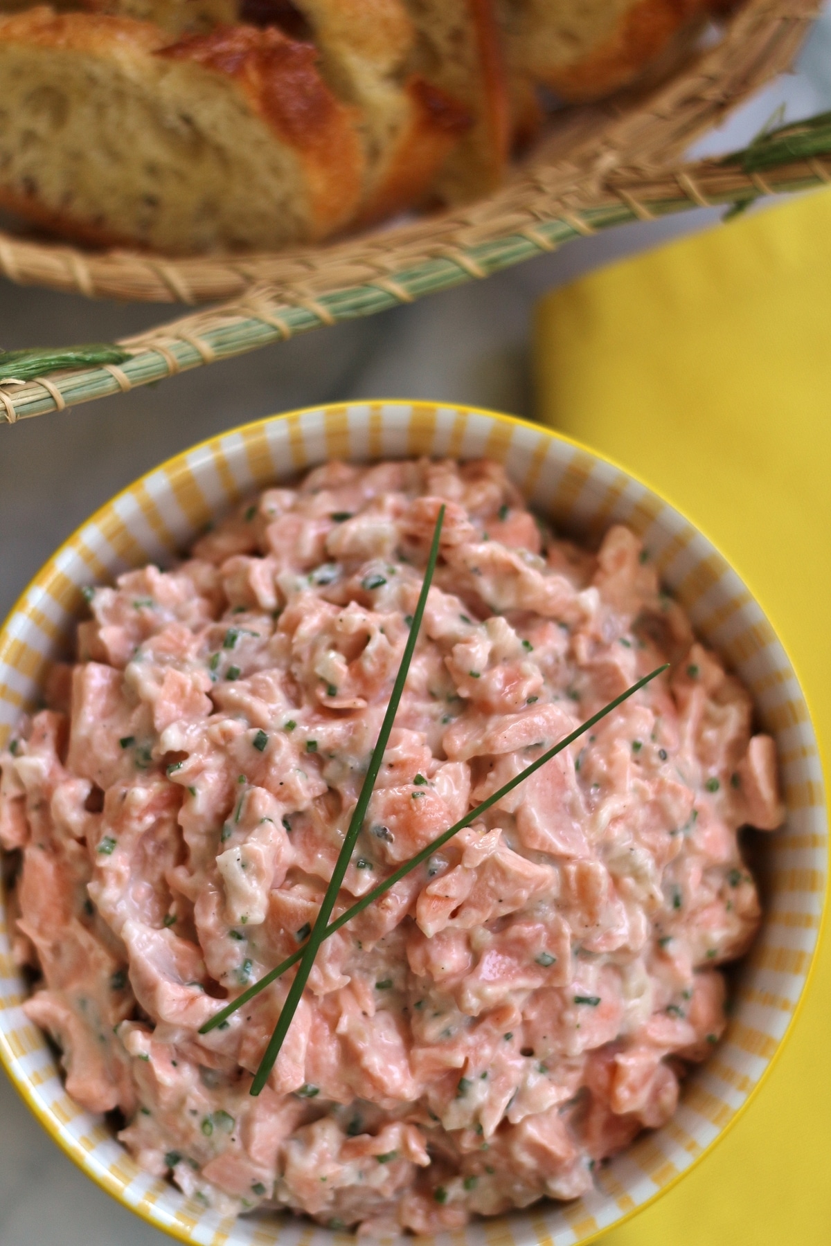 overhead view of salmon rillettes garnished with chives in a yellow bowl