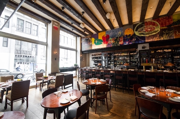 a restaurant dining room with wooden tables and a colorful mural over the bar