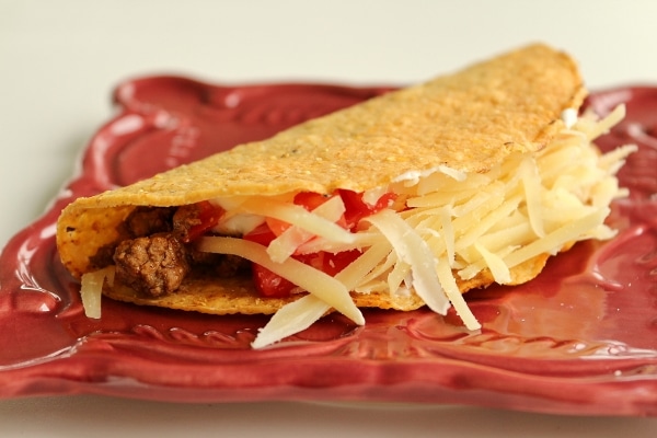 a ground beef taco with a hard shell on a square dark red plate