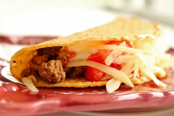 A closeup of a hard taco shell filled with ground beef, tomatoes, and cheese