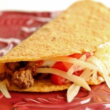 side view of a hard taco with ground beef filling on a dark red plate