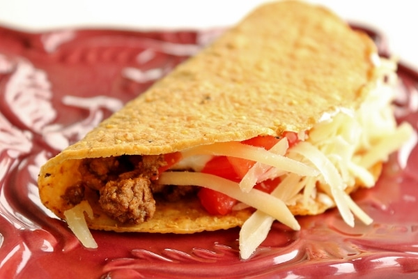 side view of a hard taco with ground beef filling on a dark red plate