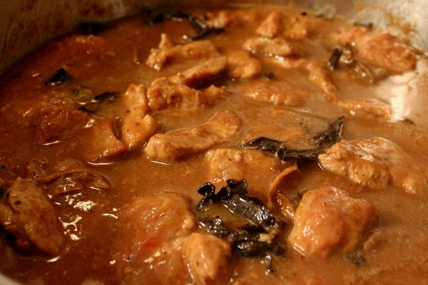 A closeup of braised meat with dark mushrooms in a metal pan