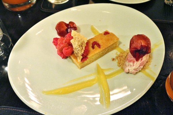 an artfully plated dessert with streaks of citrus curd and raspberries