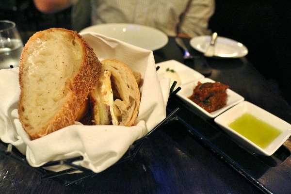 a bread basket next to a trio of spreads and dips on a black table