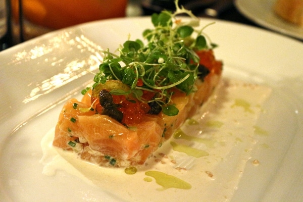 pink fish tartare shaped in a rectangle on a white plate and topped with green herbs