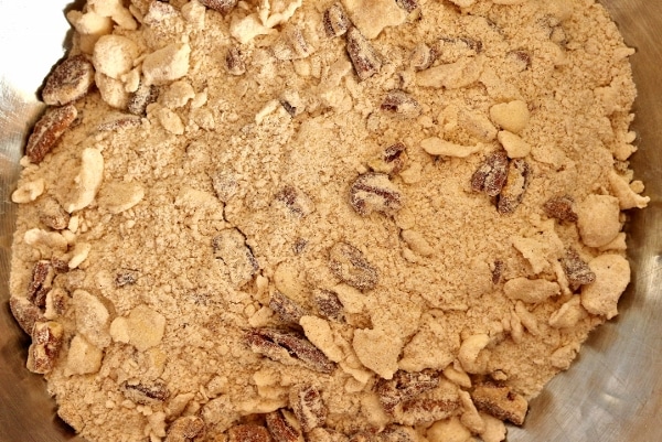 a metal mixing bowl with a crumbly dry mixture including flakes of butter and pecans
