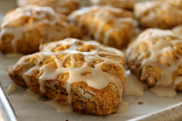 a closeup of a triangular scone with pecans and glaze drizzled over the top