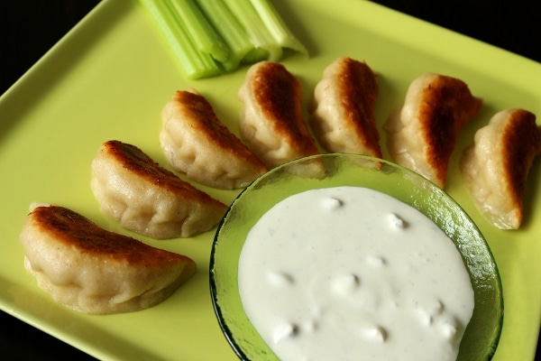 a square green plate with dumplings, blue cheese dressing, and celery sticks