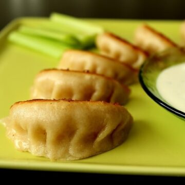 a closeup of pan-fried dumplings on a square green plate with a bowl of sauce