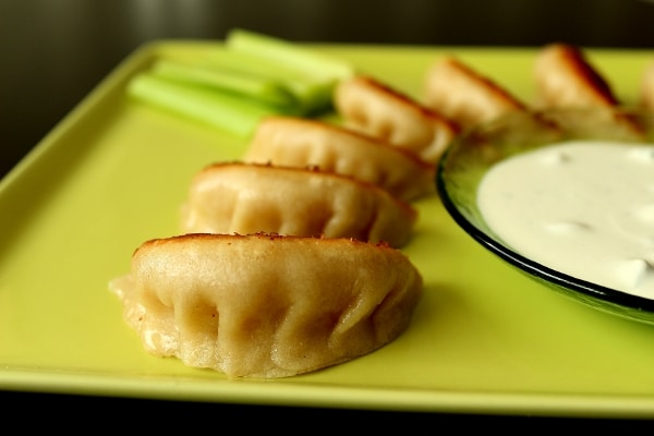 a closeup of pan-fried dumplings on a square green plate with a bowl of sauce