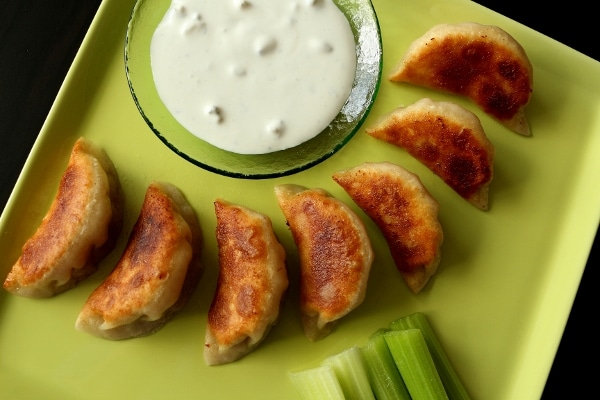 overhead closeup of pan-fried dumplings with blue cheese dressing on a square green plate