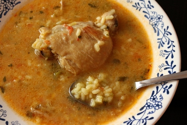 closeup of a spoonful of soupy rice in a wide bowl with a chicken thigh