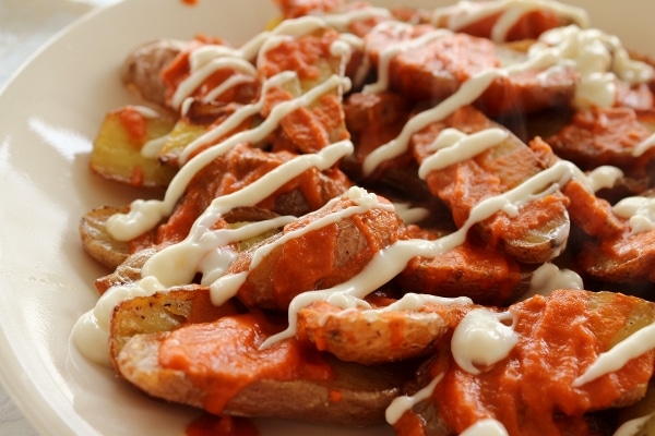 a closeup of small halved roasted potatoes topped with red and white sauces