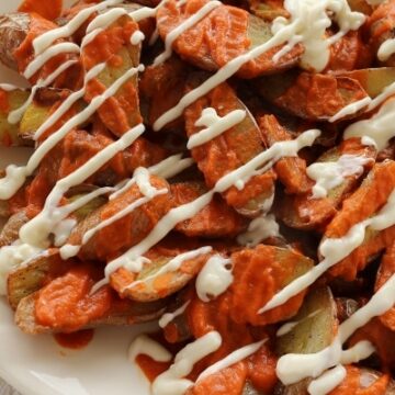 overhead view of a platter of potato pieces topped with red and white sauces