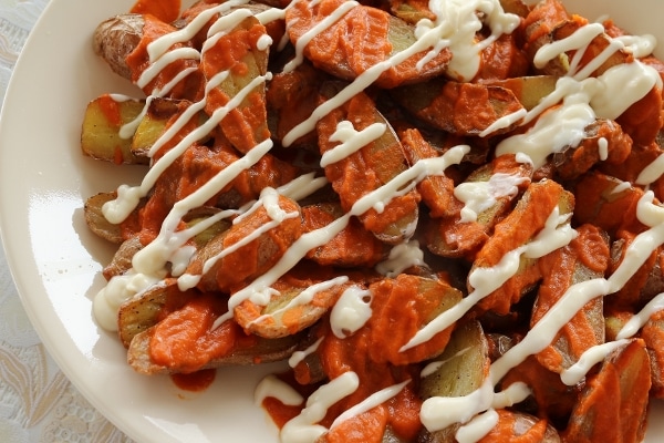 overhead view of a platter of potato pieces topped with red and white sauces