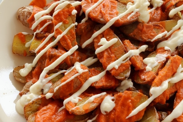 overhead close up of a platter of roasted potato pieces topped with red and white sauces