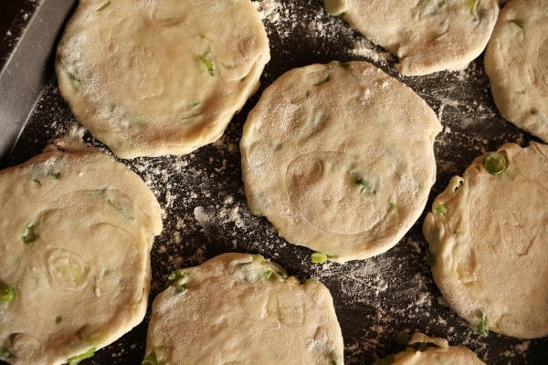 overhead view of uncooked mini scallion pancakes on a black surface