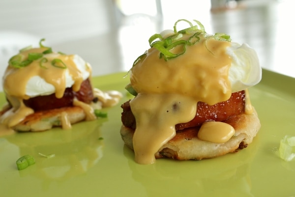 side view of an eggs benedict stack with scallion pancake and roasted pork tenderloin