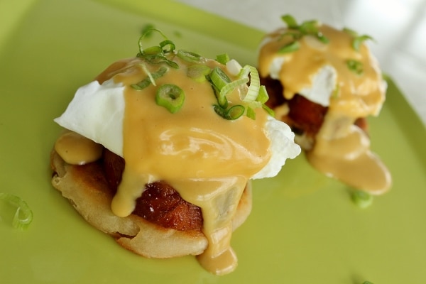 two eggs benedict stacks with hollandaise sauce on a green plate
