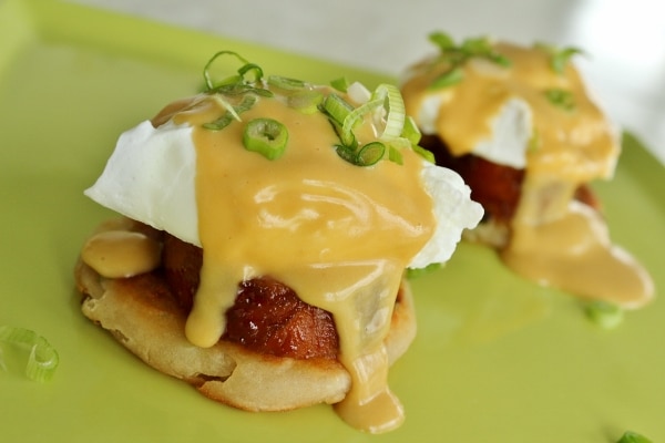 a closeup of eggs benedict with hollandaise sauce dripping down the side onto a green plate