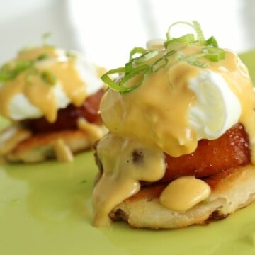 a closeup of eggs benedict with scallions on top on a green plate