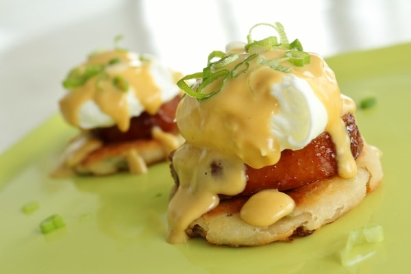 a closeup of eggs benedict with scallions on top on a green plate