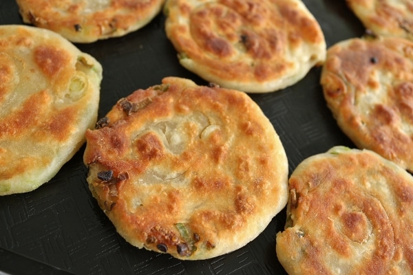 closeup of cooked mini scallion pancakes on a black surface