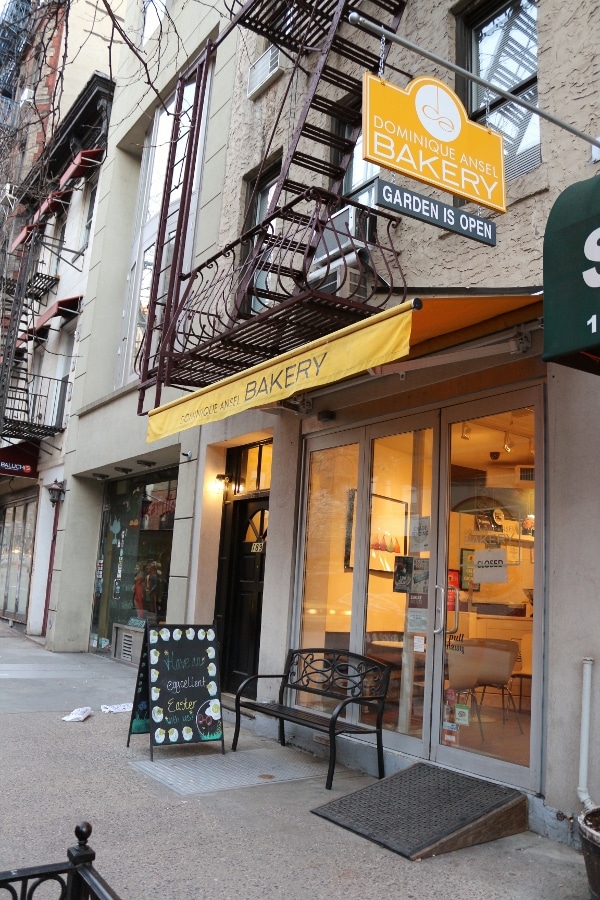 exterior of a bakery with yellow awning and a blackboard sign in front