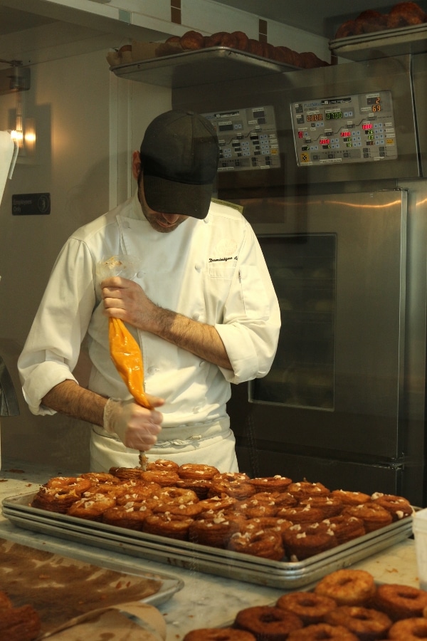 A man piping filling into doughnuts on a tray