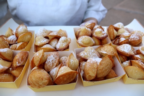 small yellow boxes of Madeleine pastries topped with powdered sugar on a white tray