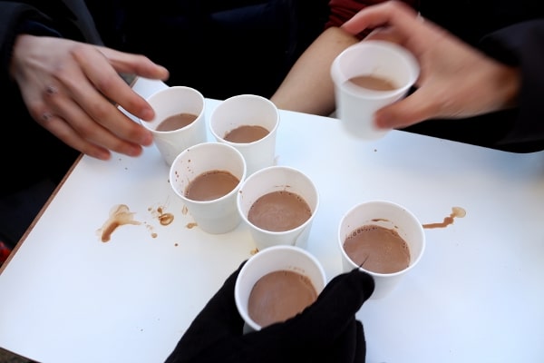 hands grabbing small paper cups of hot chocolate off a white tray