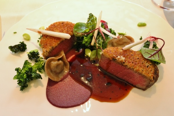 crusted beef with a tortellini, greens, and a dark brown sauce on a white plate