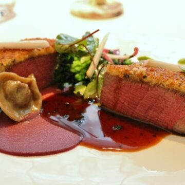 a closeup of crusted beef with a tortellini and dark brown sauce on a white plate