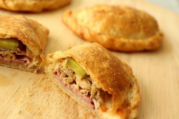 A close up of a halved Cuban sandwich empanada on a wooden board