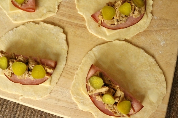 overhead view of rounds of dough on a wooden board topped with ham and pickles