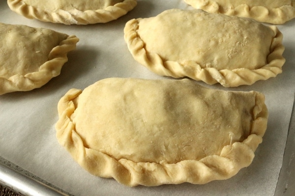 a closeup of unbaked empanadas with crimped edges on a parchment paper covered baking sheet