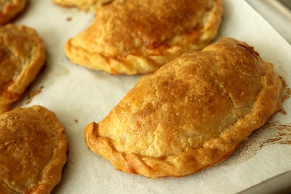 golden brown baked empanadas on a parchment paper covered baking sheet