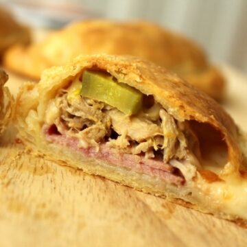 A closeup of a cross section of an empanada filled with ham, roasted pork, and pickles