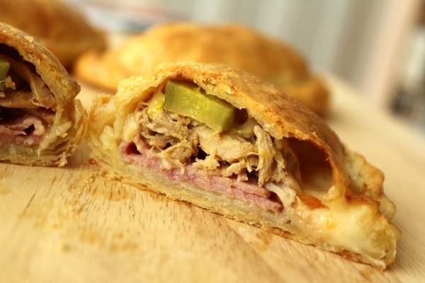 A closeup of a cross section of an empanada filled with ham, roasted pork, and pickles