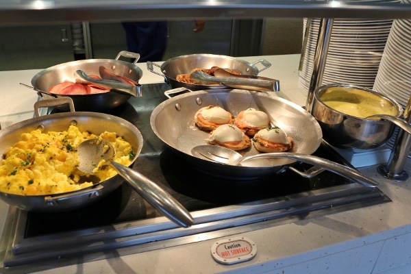 scrambled eggs and eggs benedict in metal pans on a buffet line