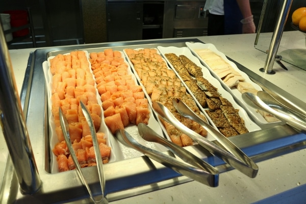 a variety of smoked fishes with metal tongs on a buffet line