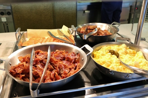 bacon, sausage, and scrambled eggs in metal pans on a buffet line
