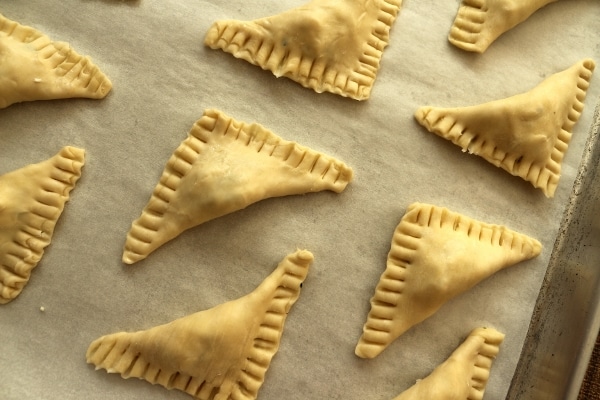 Puff pastry triangles with crimped edges, on a baking sheet ready for the oven